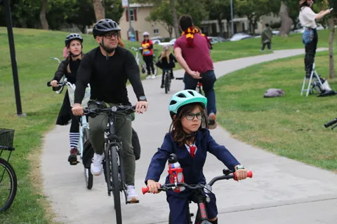 A man in a witch hat rides with two children in colorful gear.
