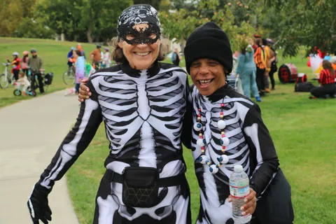 Two people in full skeleton bodysuits pose together with arms around each other, smiling.