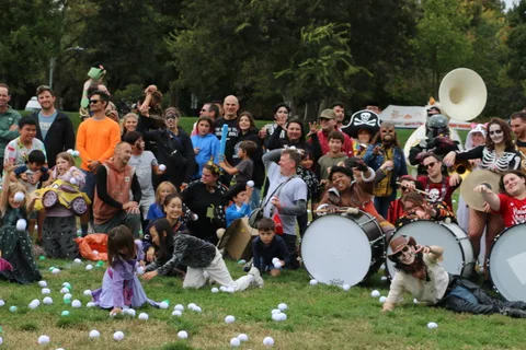 A large marching band poses with sousaphones and bass drums on the grass.