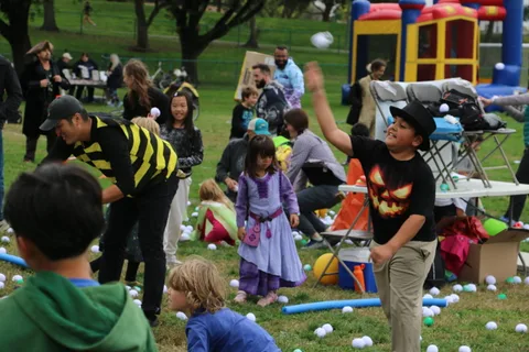 Costumed kids toss balls together on the grass.