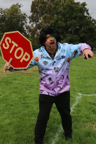 A man in costume swings a stop sign while gesturing broadly.