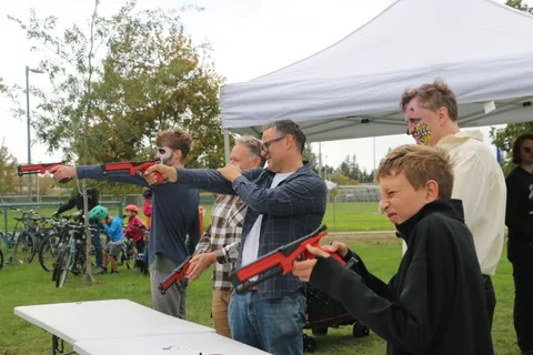 A man and a boy aim red toy blasters at each other under a white tent.