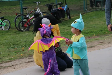 Two children in dragon and dinosaur costumes share a playful moment.