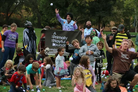 A group of costumed adults raises their hands and cheers in front of an event banner.