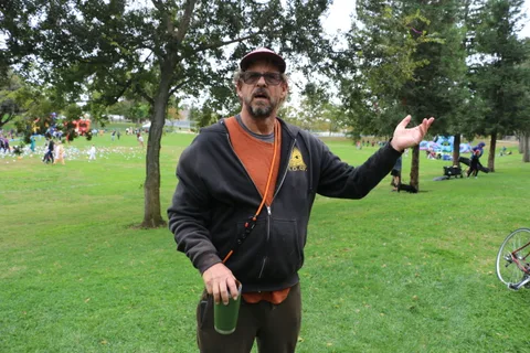 A man gestures mid-speech on the open grass.