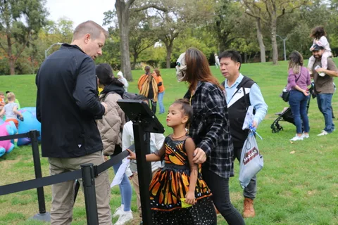 A man interviews a woman and child in costume at a busy festival scene.