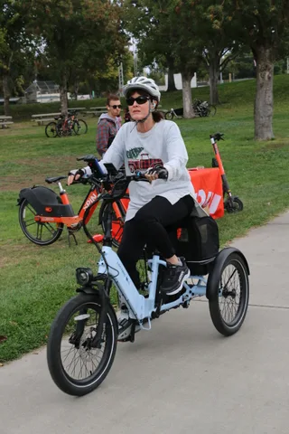 A cyclist in sunglasses rides a bike with a safety flag through the park.