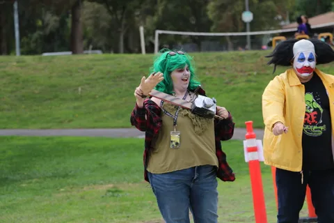 A green-haired zombie performer interacts playfully with a clown.
