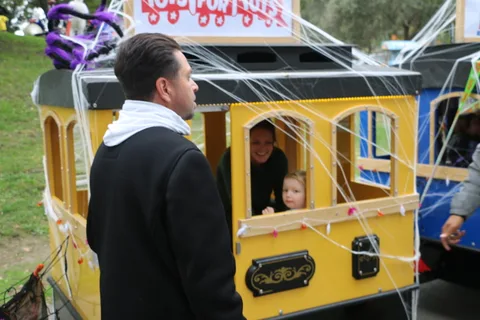 A man stands beside a decorated yellow train car with a child visible inside.