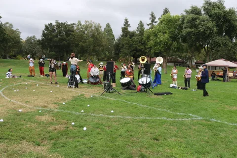A wide, mostly empty grass field with a small band setup and cloudy sky in the distance.