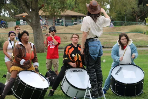 A performer stands on a ladder above a colorfully costumed crowd.