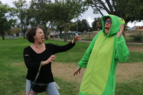 A woman gestures animatedly beside a person wearing a green frog costume.