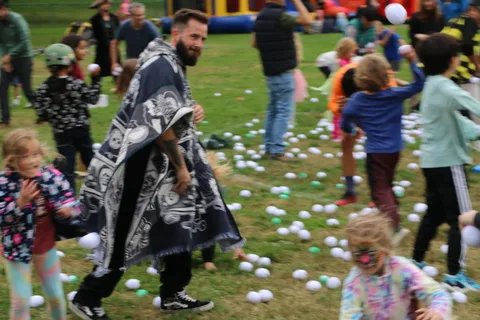 A man in a dark hooded robe leaps mid-motion as balls fly through the air.