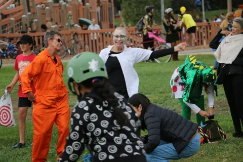A group in orange jumpsuit costumes interacts with a green dinosaur mascot.