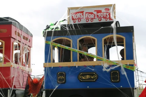 A blue trolley car decorated with spiderwebs carries a Toys for Tots banner.