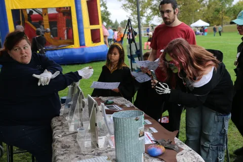 A zombie-costumed visitor reaches for a pamphlet at a booth table.