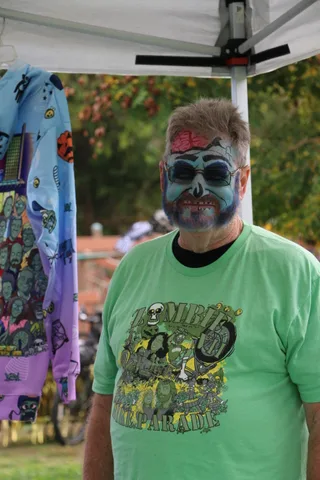 A man's zombie makeup features red markings above the brow in this close portrait.