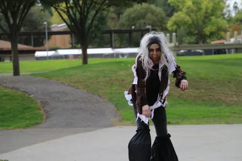 A zombie performer in tattered robes walks straight toward the camera.