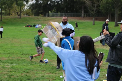A person in a box costume reaches toward another costumed figure holding a ball.