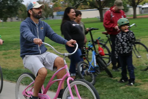 A man on a pink cruiser bike rides past a costumed crowd.