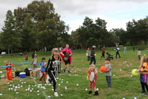 A child in a skeleton costume runs across a grassy field scattered with white balls.