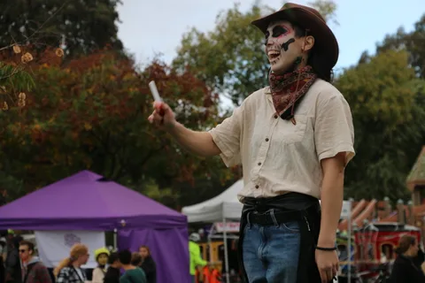 A man in skeleton face paint points playfully with a drumstick.