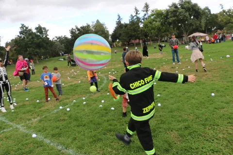 A large striped ball flies through the air as a boy in a firefighter costume reaches for it.