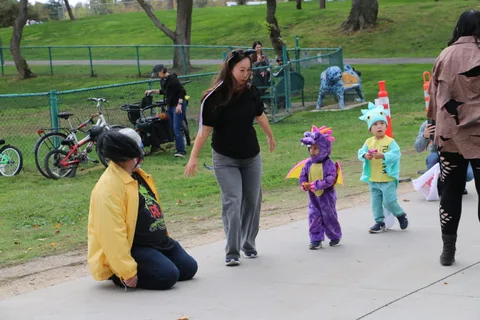 Children in dragon and dinosaur costumes walk near a zombie performer.
