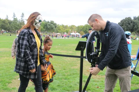 A woman in skull face paint and a girl in a butterfly costume stand near a camera rig.