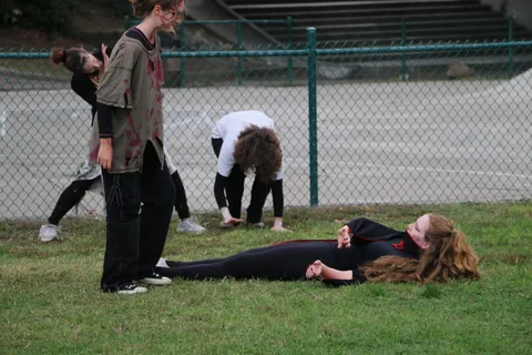 Performers gather around a costumed figure lying in the grass.