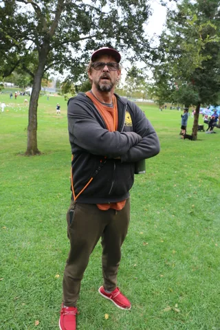 A man in a zip jacket stands with his arms crossed on the grass.