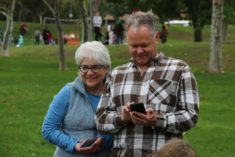 An older woman and a man look together at a phone in the park.