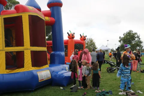 Children gather around a red and blue inflatable bounce house castle.