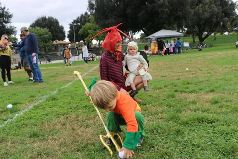A boy in an orange costume kneels down while holding a trident.