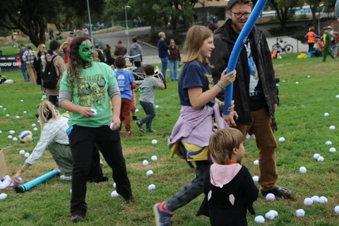 A woman with green face paint stands with a girl holding a pool noodle.