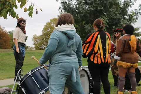 A wide scene of costumed people seen from behind pushing a drum cart.