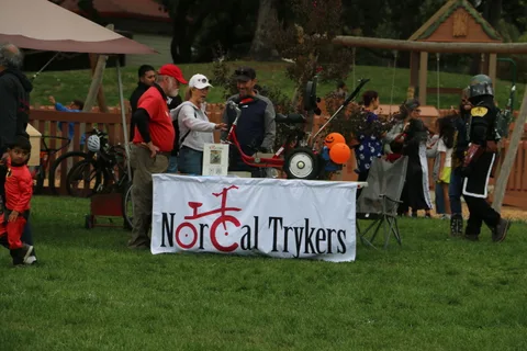 Volunteers set up a booth with a NorCal Trykers banner and adaptive trikes on display.
