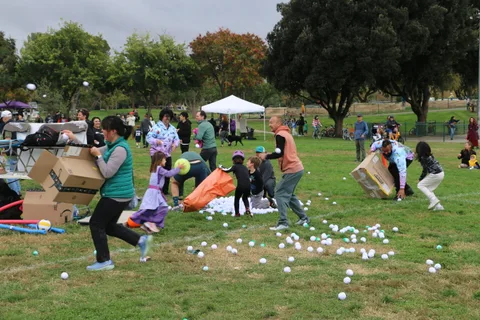 A costumed woman runs across the grass among scattered play balls.