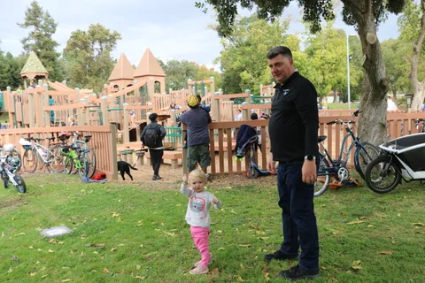 A man stands on the grass near a playground while a child plays nearby.