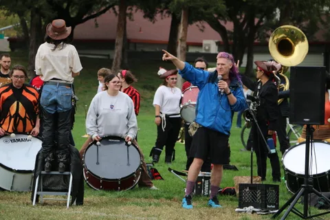 A young performer sings as a tuba player and drummer perform nearby.