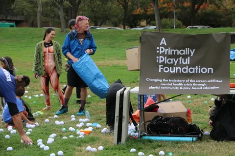 Two costumed figures toss white balls onto the grass near a foundation banner.
