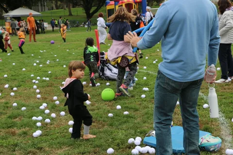 A man crouches down to interact with a toddler in a pink outfit.