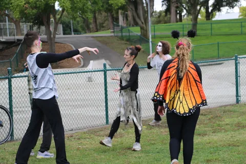 A small group in zombie makeup and a monarch butterfly costume gathers on a park path.