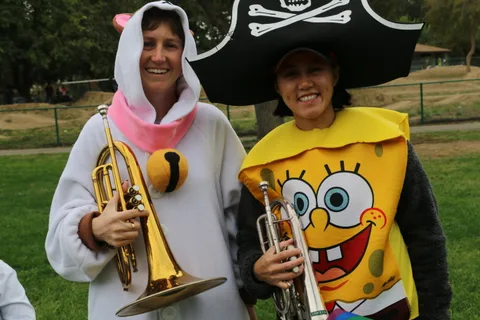 Two women in cartoon sponge costumes hold trumpets and smile broadly.