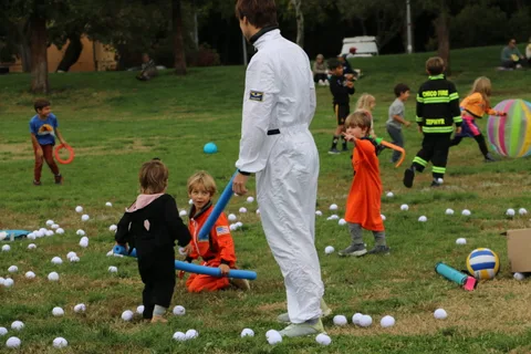 An astronaut-costumed adult stands with a group of children in matching orange jumpsuits.