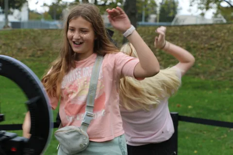 A teenage girl laughs with her arm raised at the ring-light photo booth.
