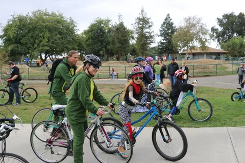 A family in green dinosaur costume walks bikes together on the path.