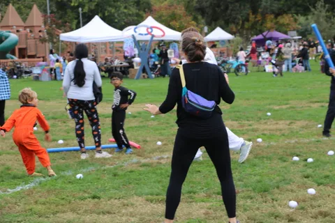 A woman and a running child pass by scattered balls and boxes at the festival.