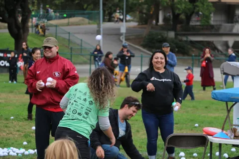 Two women crouch and throw white balls at each other, laughing.