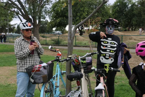 A man drinks from a cup while standing next to his bicycle in the park.